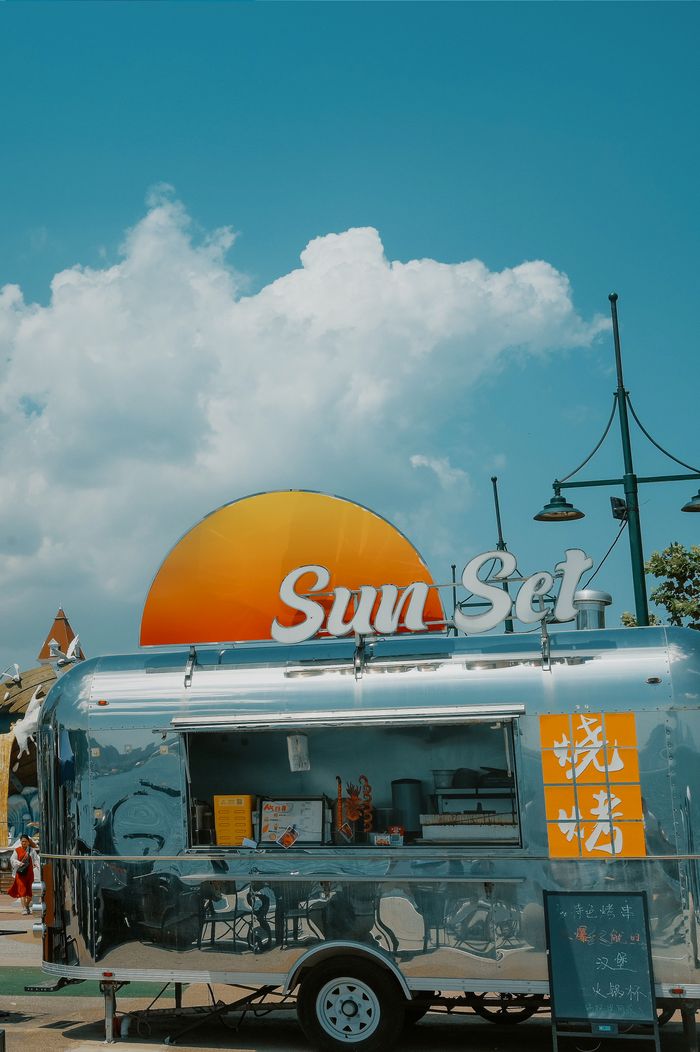 contact-img A vibrant food truck shines under a bright blue sky with a sunset sign.